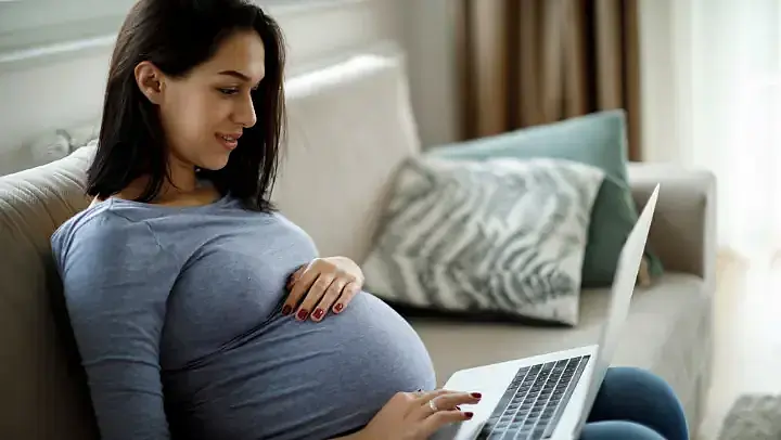 Schwangere Frau recherchiert am Laptop