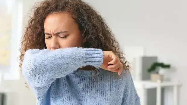 Junge Frau hustet in die Armbeuge.