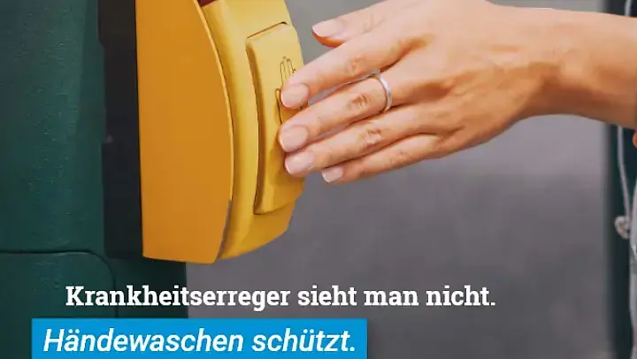 Ausschnitt aus einem Plakat der Kampagne „Wo waren deine Hände heute?“ Eine Hand kommt von rechts ins Bild und betätigt den Warteknopf an einer Ampel. Darunter der Slogan: „Krankheitserreger sieht man nicht. Händewaschen schützt.“