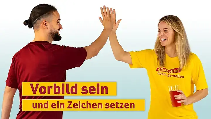 Ein Mann (links im Bild, zu sehen von schräg hinten) und eine Frau (rechts im Bild, zu sehen von vorne) schlagen ein. Die Frau hält ein rotgefärbtes Getränk in der Hand. Slogan unten links: „Vorbild sein und ein Zeichen setzen“