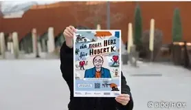 Person, die man nicht sieht, hält Plakat mit GraphicNovel "Neues Herz für Hubert K." hoch