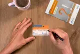 Tisch in der Draufsicht, darauf zentral zwei Hände, die einen Organspendeausweis ausfüllen. Außerdem im Anschnitt ein Flyer zum Thema Organspende und ein halb gefüllte Kaffeetasse