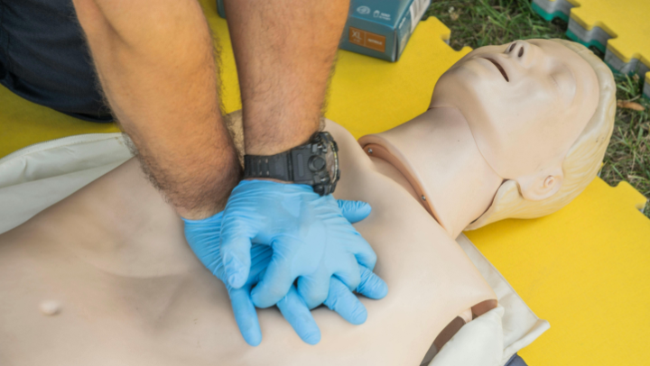 Hände mit blauen Einweghandschuhen führen auf Trainingspuppe eine Herzdruckmassage durch.