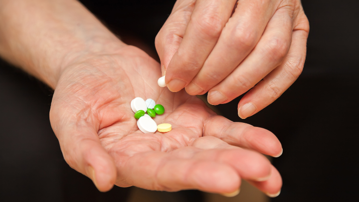 Zwei Hände: Eine ist zur Schale geformt, darin liegen Tabletten. Die andere Hand nimmt eine derTabletten.