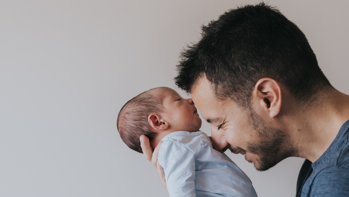 Nahaufnahme eines jungen Mannes, der ein Baby hält und es liebevoll mit der Nase anstupst. 