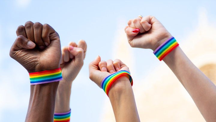 Vier gen Himmel gestreckte Fäuste, jeweils mit Regenbogenarmbändern. 