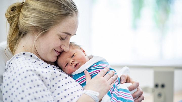 Mutter mit neugeborenem Baby, das in ein Handtuch gewickelt auf ihrer Brust liegt.