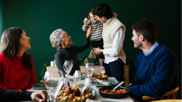 Zu sehen ist eine Familien bei einer Feier. Sie essen gemeinsam am Tisch und lachen zusammen.